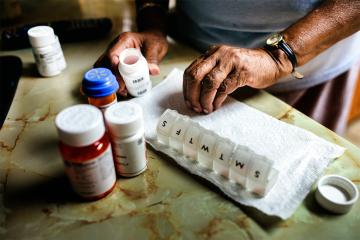 a senior citizen refills a medication dispenser with various medications