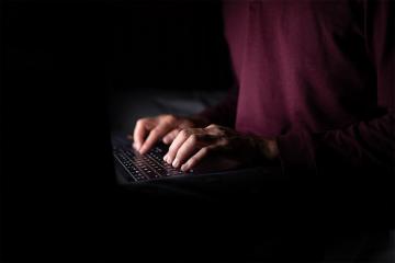 white hands typing on a laptop in a darkened room