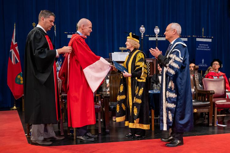 Chuck O’Reilly hoods David Denison with Chancellor Patten and President Meric Gertler on stage