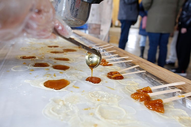 Maple syrup is poured out of a metal ladle. 