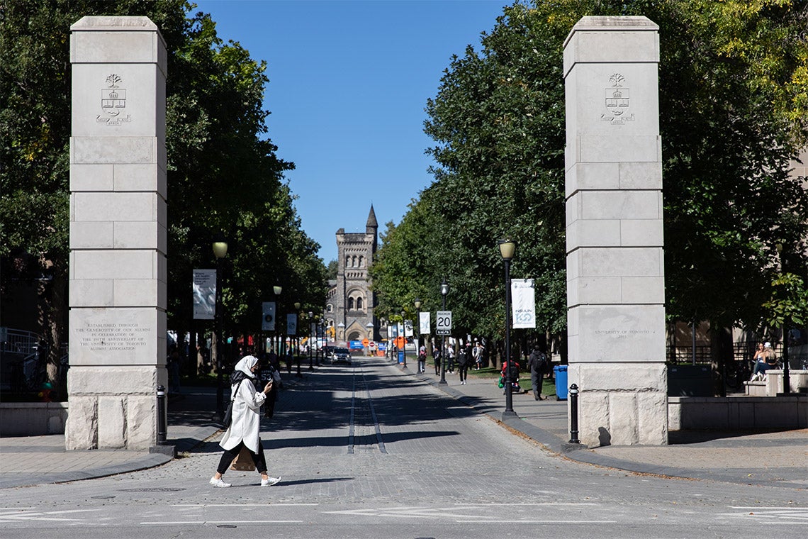 A woman walks past the King's College Gate at the University of Toronto
